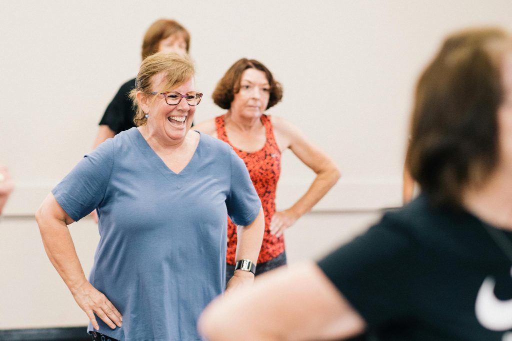 Happy middle-aged women participating in an indoor fitness class, promoting health and social interaction.