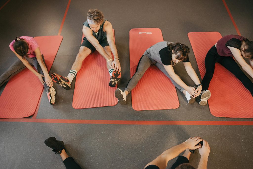 Four people stretching on red mats during a group exercise session indoors.