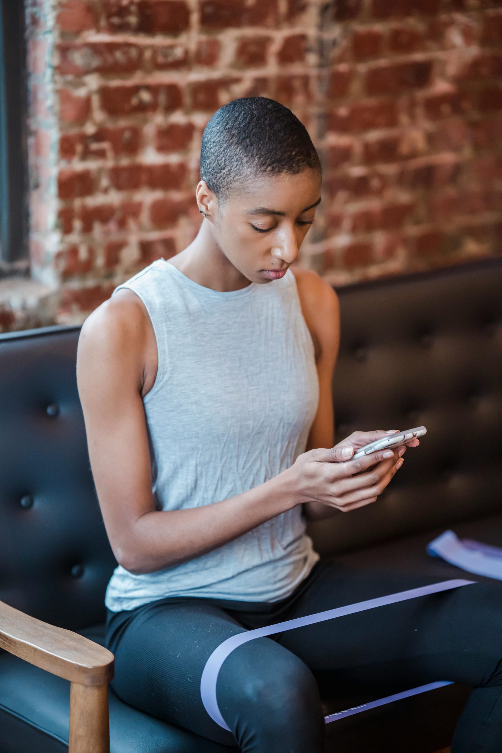 High angle of focused African American female sitting on sofa and watching video on mobile phone during training with fitness band