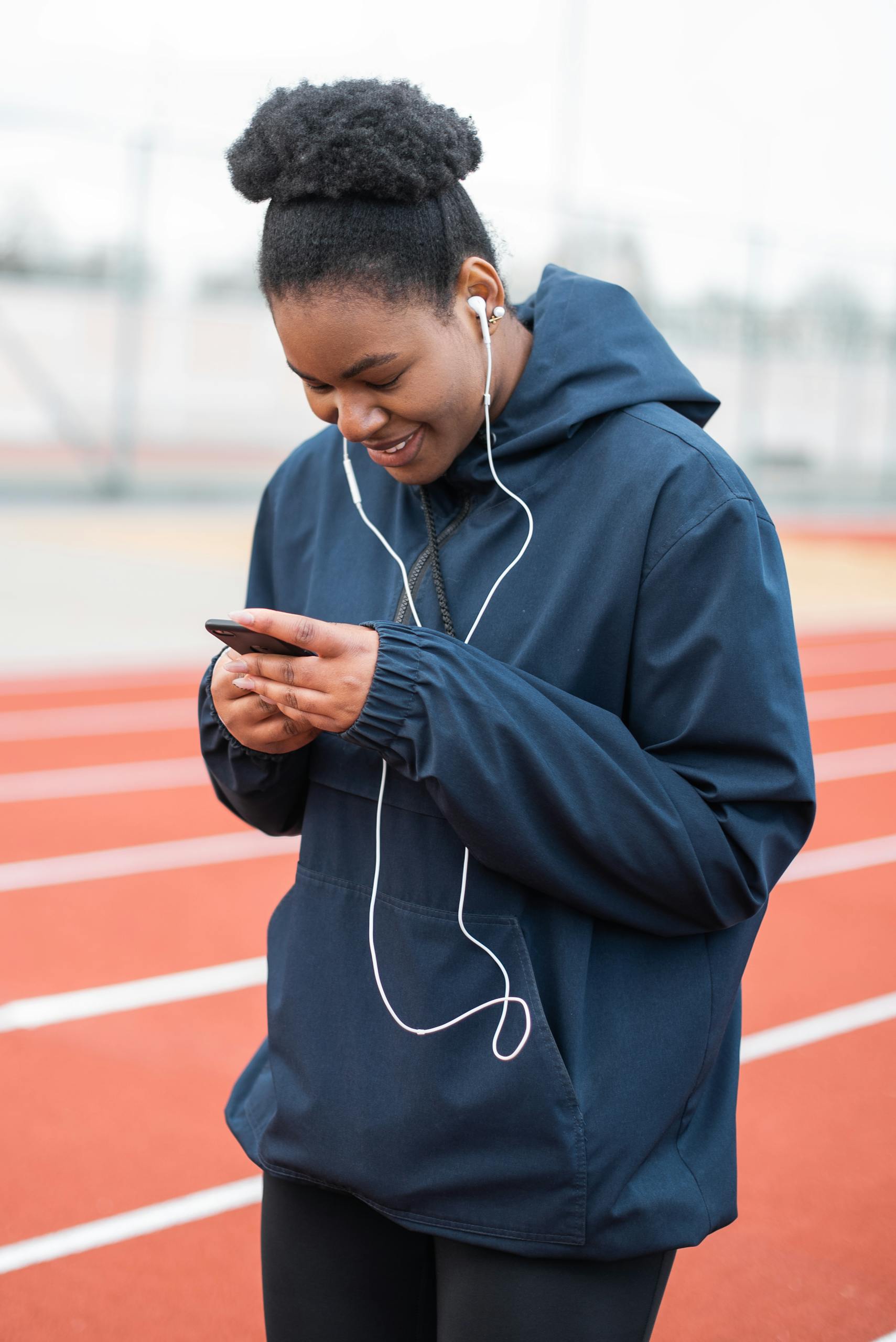 Smiling woman in sportswear listens to music on track field.